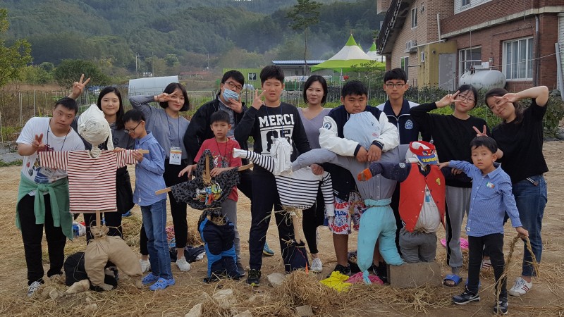 허수아비 만들기 프로그램에 참여하고 있는 가족캠프 참여 자녀들과 자원봉사자 사진 